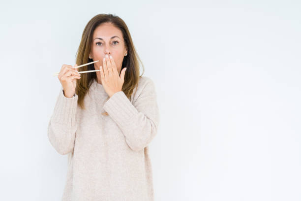 Middle age woman holding asian chopsticks over isolated background cover mouth with hand shocked with shame for mistake, expression of fear, scared in silence, secret concept Middle age woman holding asian chopsticks over isolated background cover mouth with hand shocked with shame for mistake, expression of fear, scared in silence, secret concept how do you say shut up in japanese stock pictures, royalty-free photos & images
