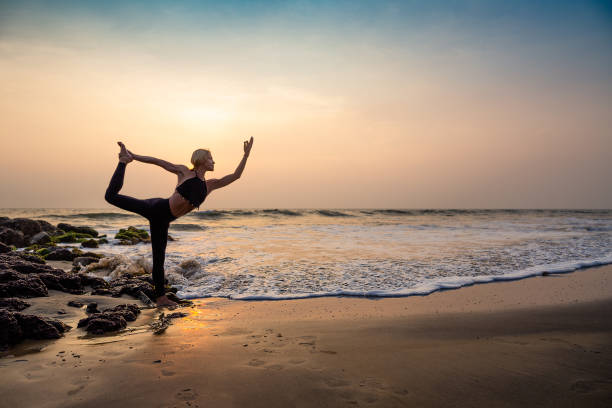 Middle age woman in black doing yoga on sand beach in India stock photo