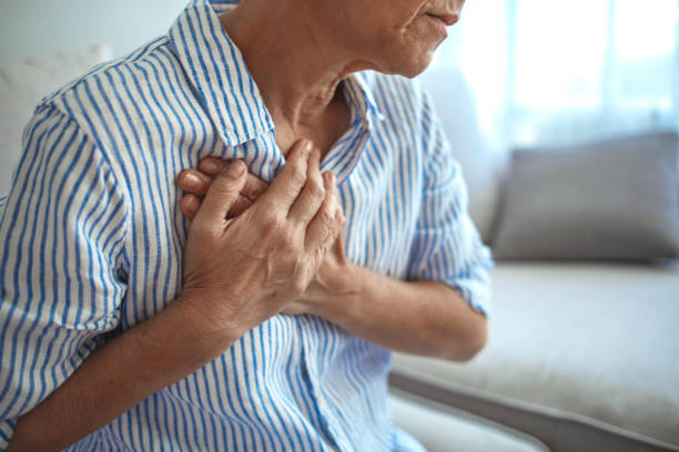 Middle age woman wheezing touching chest at home Senior Woman Suffering From Chest Pain While Sitting on Sofa at Home. Portrait of Elderly Woman Having Heart Attack. Heart problems can affect anyone at any time condition stock pictures, royalty-free photos & images