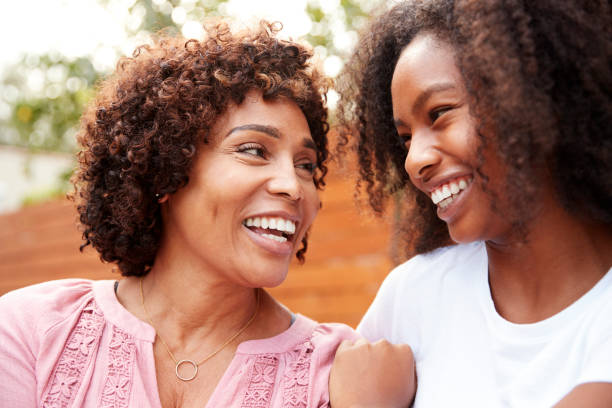 middle aged black mum and teen daughter smiling at each other - mother and daughter imagens e fotografias de stock