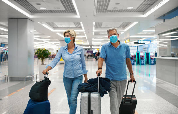Middle aged couple at an airport during coronavirus pandemic. Closeup front view of a mid 50's couple waiting for a flight after coronavirus travel ban has been lifted. Both wearing face mask while walking through almost empty airport. passenger stock pictures, royalty-free photos & images