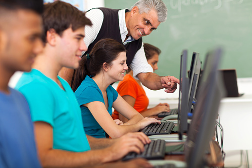 Middle Aged Teacher Teaching Computer To Students Stock
