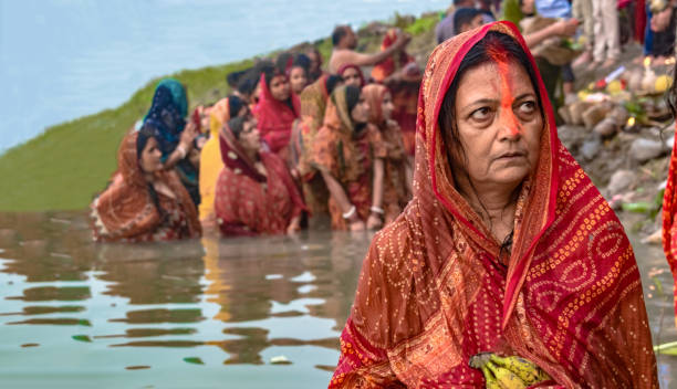 Middle Aged Woman in Ethnic Indian Wear with Sindoor (Vermilion) on head, celebrating Chhath Puja, taking holy dip in River Ganges and giving offerings to Sun God. Middle aged Indian woman with vermilion on her forehead, draped in the traditional Red ethnic saree taking part in the ritual of Chhath puja, a very famous festival widely celebrated in the Eastern India. The festival is celebrated to thank the Sun God as He is the source of all form of energies available on mother earth. She observed the fast of whole day and is waiting for the sun to rise the next day with offerings, while taking a holy dip in the River Ganges. chhath stock pictures, royalty-free photos & images