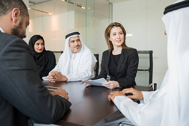 Middle Eastern business people in meeting at office A photo of multi-ethnic business people looking at colleague. Some are in formalwear and others are wearing traditional clothes. Caucasian woman is sitting at conference table with Arab colleagues during meeting. Dubai, United Arab Emirates. dubai stock pictures, royalty-free photos & images