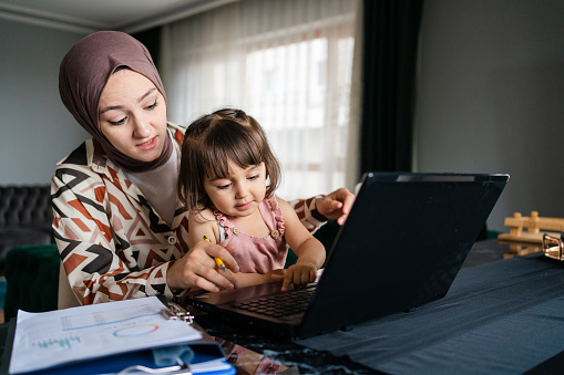 Middle Eastern mother working and spending time with baby at home