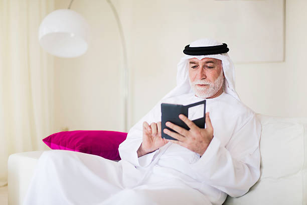 Middle eastern senior with phone at home dressed in dishdasha. Middle eastern senior with phone at home dressed in dishdasha. old arab man stock pictures, royalty-free photos & images