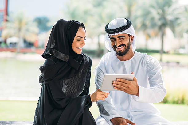 Middle Eastern young people with digital tablet smiling Young smiling man showing content on digital tablet to young smiling woman, The people are with traditional arabic clothes. agal stock pictures, royalty-free photos & images