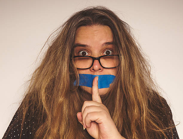 Middle-age woman with mouth taped Middle-age woman with mouth taped and holding a finger to her mouth human mouth gag adhesive tape women stock pictures, royalty-free photos & images