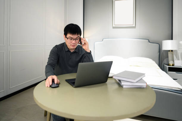 A middle-aged Asian white-collar man works from home and uses his mobile phone. stock photo