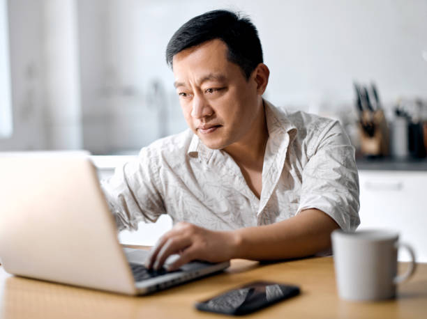 Middle-aged man freelancer using laptop studying online working from home Middle-aged man freelancer using laptop studying online working from home， happy casual millennial guy typing on pc notebook surfing internet looking at screen enjoying distant job sit at table east asian culture stock pictures, royalty-free photos & images
