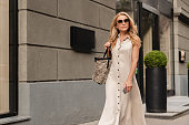istock Middle-aged mature woman with blond hair wearing sunglasses walking on city streets while doing shopping outdoors. Sales and discounts concept. 1338720994