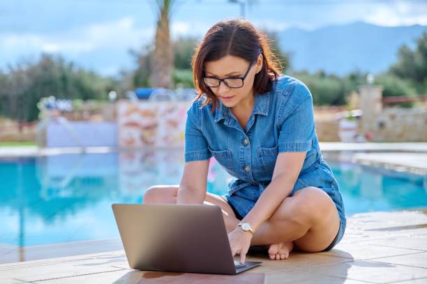Middle-aged woman relaxing near the pool using a laptop. stock photo