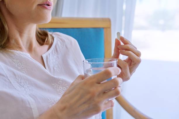 Middle-aged woman taking pill at home in chair stock photo