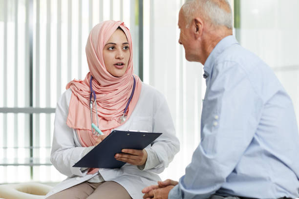 Middle-Eastern Doctor Talking to Patient Portrait of young Arab woman working as doctor in medical clinic and talking to senior patient filling in form on clipboard, copy space old arab man stock pictures, royalty-free photos & images