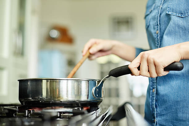 Midsection image of woman cooking food in pan Midsection below view image of woman cooking food in pan. Utensil is placed on gas stove. Female is stirring dish in frying pan. She is preparing food in domestic kitchen. cooking pan stock pictures, royalty-free photos & images