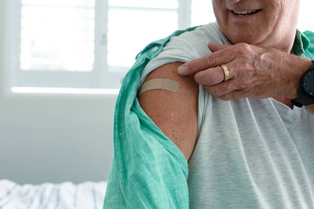 Midsection of smiling caucasian senior man with plaster on arm after vaccination stock photo
