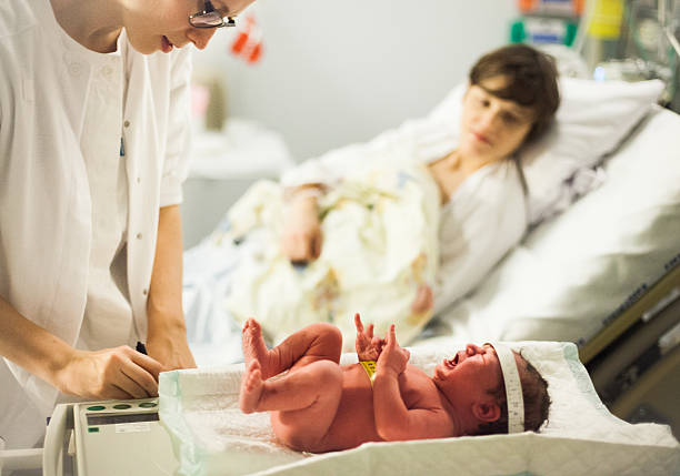 Midwife, mother and newborn baby Calm and patient midwife weighs a screaming and crying newborn baby, mother in background midwife stock pictures, royalty-free photos & images