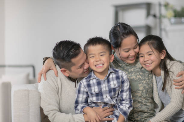 Military Family Sitting On Couch A family of four is happily sitting on the sofa in their living room. The mother has just returned home from serving her country and is wearing a military uniform. filipino family stock pictures, royalty-free photos & images