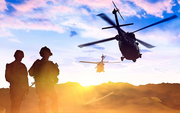 Military Helicopter and Army Soldiers at sunset A military helicopter flies over troops on the ground at sunset. military helicopter stock pictures, royalty-free photos & images