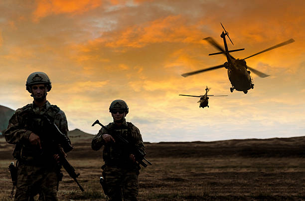 Military Mission on sunset Two soldiers walking in the battlefield while two military helicopter flying over them during a military operation at sunset. military helicopter stock pictures, royalty-free photos & images