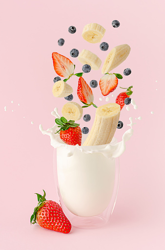 Fresh summer fruits and berries flying over the splashing milk on pink background. Milkshake levitation