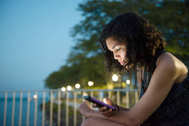 Millennial Hispanic Woman On Social Media in Chicago Park Night A beautiful, millennial Puerto Rican woman in her 20's sits in a park in Chicago, Illinois, a major USA city in the Midwest. She looks at her phone spending time on social media. The light from the phone illuminates her face at night. hot puerto rican woman stock pictures, royalty-free photos & images