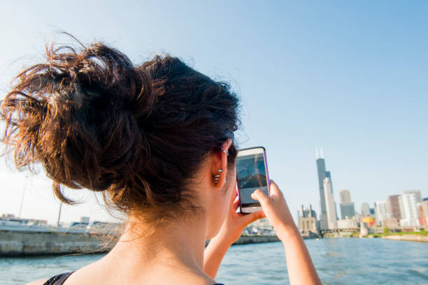Millennial Hispanic Woman Takes Photograph of Chicago Skyline A beautiful, millennial Puerto Rican woman in her 20's stands by the Chicago River on a boat in Chicago, Illinois, a major USA city in the Midwest. She looks at her phone as she takes a photograph of the famous skyline with her mobile phone. hot puerto rican woman stock pictures, royalty-free photos & images