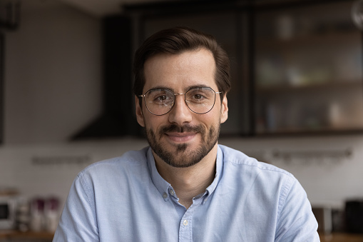 Portrait of young smiling handsome bearded man in glasses looking at camera chatting with wife friend by videocall. Millennial male team leader organize virtual meeting workshop with employees online