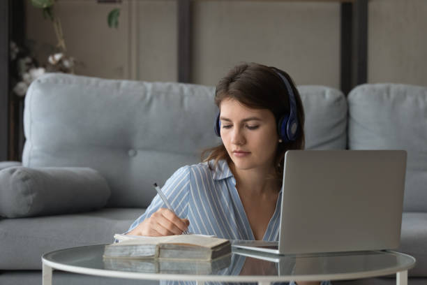 Millennial remote student girl in earphones studying at home stock photo