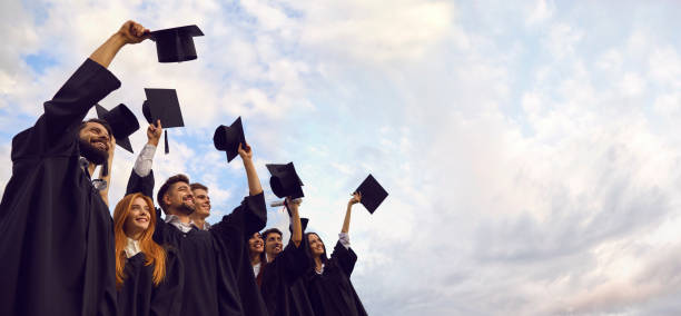 Millennial students celebrating graduation ceremony and throwing their caps up. Young people on commencement day stock photo