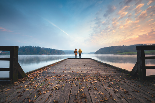 Young couple standing on the jetty and watching sunrise.