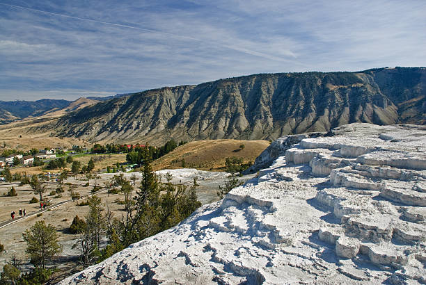 Minerva Terrace and Mammoth Hot Springs Minerva Terrace is the most famous feature of the Mammoth Hot Springs complex. It is a series of travertine terraces on a hill close to the historic Fort Yellowstone. The hot springs were created over thousands of years as hot water from the spring cooled and deposited calcium carbonate. The hot water that feeds Mammoth Hot Springs travels underground from Norris Geyser Basin via a fault line. The limestone from rock formations along the fault is the source of the calcium carbonate. Algae living in the warm pools have tinted the travertine shades of brown, orange, red, and green. Due to recent earthquake activity, the spring has shifted causing the terraces to become dry. Mammoth Hot Springs is in Yellowstone National Park, Wyoming, USA. jeff goulden yellowstone national park stock pictures, royalty-free photos & images
