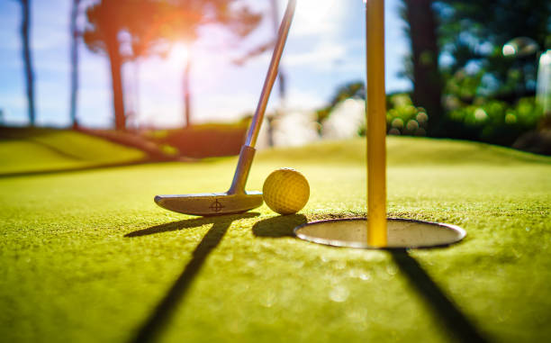 Mini Golf yellow ball with a bat near the hole at sunset stock photo