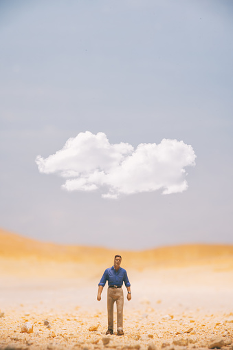 A miniature man standing in the desert with a white cloud overhead.