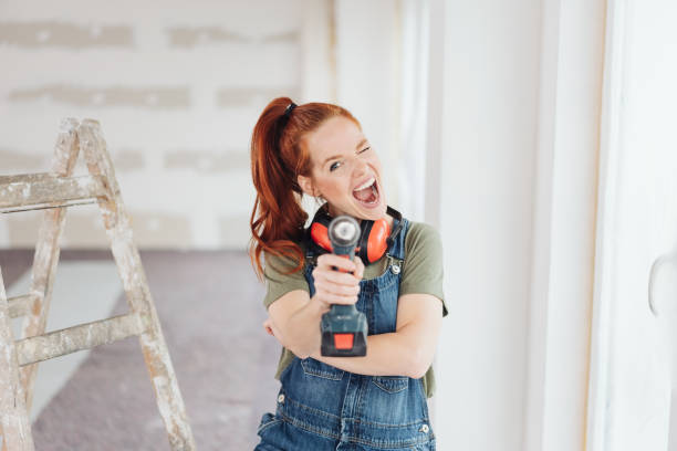 Mischievous woman shooting the camera Mischievous woman shooting the camera aiming a handheld power drill during home renovations diy stock pictures, royalty-free photos & images