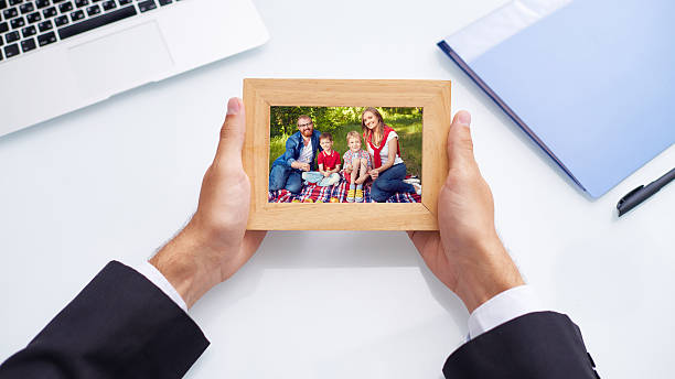 Missing my family Hands of man holding family photo over office desk desk photos stock pictures, royalty-free photos & images