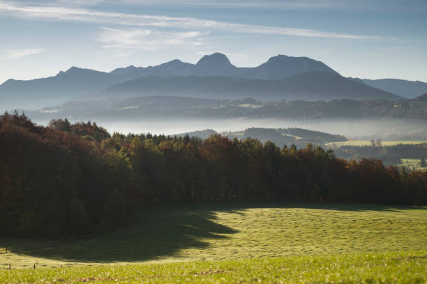Mist in the valleys and colourful autumnal forests of the Bavarian alps with Mount Wendelstein seen from Mount Irschenberg in the morning sun, Germany stock photo