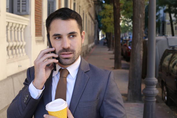 Mistrustful looking businessman answering phone call outdoors stock photo