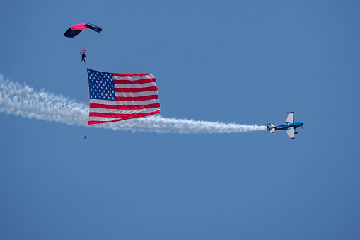 Hillsboro, Oregon, USA - May 22, 2022 :  Misty Blues, an all women skydiving team with the American flag. Melissa Burns in her Edge 540 aerobatic airplane is flying around the Misty Blues. The Air Show in Hillsboro, Oregon is a very popular event each year. The theme for 2022 was “She Flies with her own wings.” All performers, pilots and announcers were women. Hillsboro is a suburb of the city of Portland, Oregon.