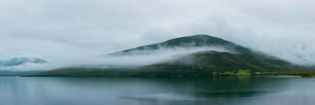 A Misty Lake With Rolling Fog Against a Green Mountain Background stock photo