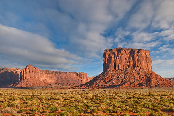Mitchell Butte and Gray Whiskers in the Evening Light Monument Valley, on the Arizona - Utah border, gives us some of the most iconic and enduring images of the American Southwest. The harsh empty desert is punctuated by many colorful sandstone rock formations. It can be a photographer's dream to capture the ever-changing play of light on the buttes and mesas. Even to the first-time visitor, Monument Valley will probably seem very familiar. This rugged landscape has achieved fame in the movies, advertising and brochures. It has been filmed and photographed countless times over the years. If a movie producer was looking for a landscape that epitomizes the Old West, a better location could not be found. This picture of Mitchell Butte and Gray Whiskers in the evening light was photographed from the Monument Valley Road north of Kayenta, Arizona, USA. jeff goulden landscape stock pictures, royalty-free photos & images