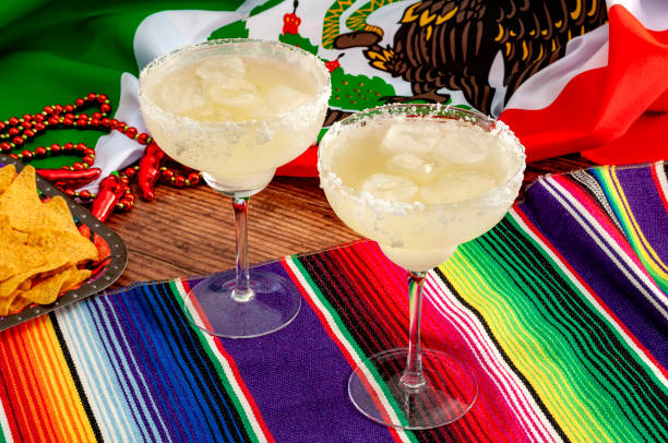 Mixed alcoholic drinks and spirits, patriotic party and Mexican fiesta concept theme with two margarita glasses with salted rim, tortilla chips and the flag of Mexico on traditional rug called serape stock photo