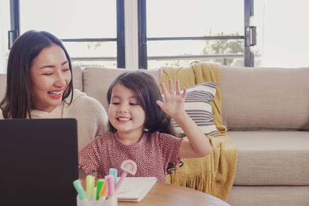 Mixed Asian girl making video calling with laptop with her mother at home, using zoom online virtual class , social distancing, homeschooling, remotely  learning during covid pandemic, new normal concept stock photo