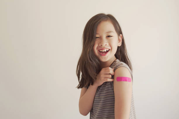 Mixed Asian young girl showing her arm with pink bandage after got vaccinated or  inoculation, child immunization, covid delta vaccine concept stock photo