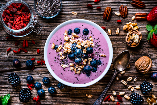 Healthy eating: overhead view of a mixed berries smoothie bowl with oat, chia seeds and nuts shot on rustic wooden table. Blackberries, blueberries, goji berries, pecan, walnuts and chia seeds are around the smoothie bowl. High resolution 42Mp studio digital capture taken with Sony A7rII and Sony FE 90mm f2.8 macro G OSS lens