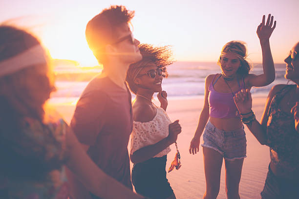 Mixed race group of friends dancing together at a beachparty Mixed race group of joyful friends dancing together on a summer evening at a beachparty adolescence photos stock pictures, royalty-free photos & images