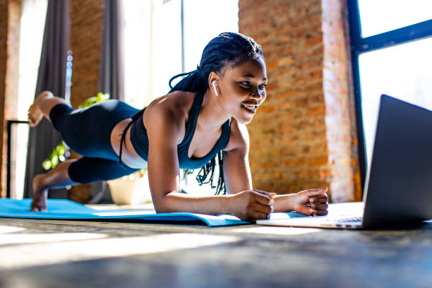 mixed race healthy woman in black sporty suit during her fitness workout at home against the background of panoramic windows sunlight stock photo