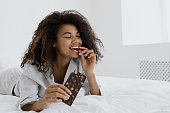 istock Mixed race woman eating milk chocolate in bed 1355161407