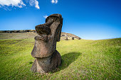 Ultra wide angle 10mm shot of Easter Island Moai Statue at Rano Raraku, on green grass volcanic hills under sunny deep blue summer sky. Rano Raraku, Rapa Nui National Park, Hanga Roa, Easter Island, Chile.