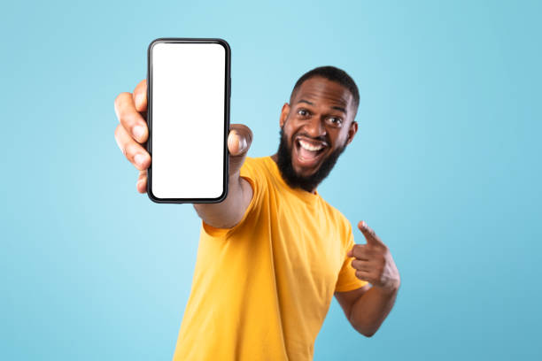 Mobile app advertisement. Excited black man pointing at smartphone with empty screen, mockup. Space for ad or website stock photo